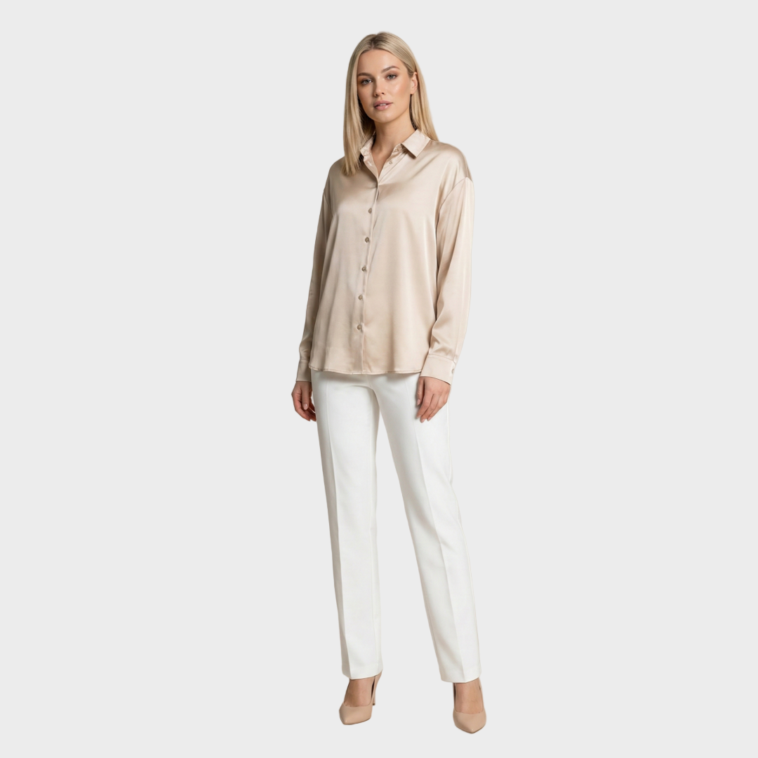 Woman wearing a beige blouse and white pants against a plain background